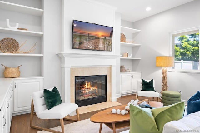 living area with a tiled fireplace, hardwood / wood-style floors, and built in shelves