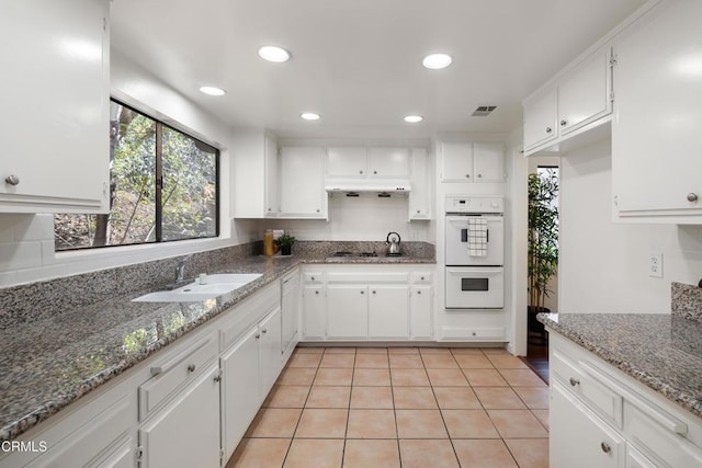 kitchen with stone countertops, double oven, white cabinetry, sink, and light tile patterned floors