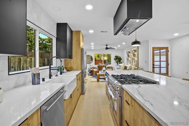 kitchen with pendant lighting, light stone counters, ceiling fan, stainless steel appliances, and wall chimney exhaust hood