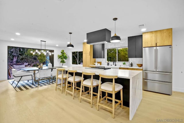 kitchen featuring stainless steel appliances, light stone countertops, light hardwood / wood-style flooring, and decorative light fixtures