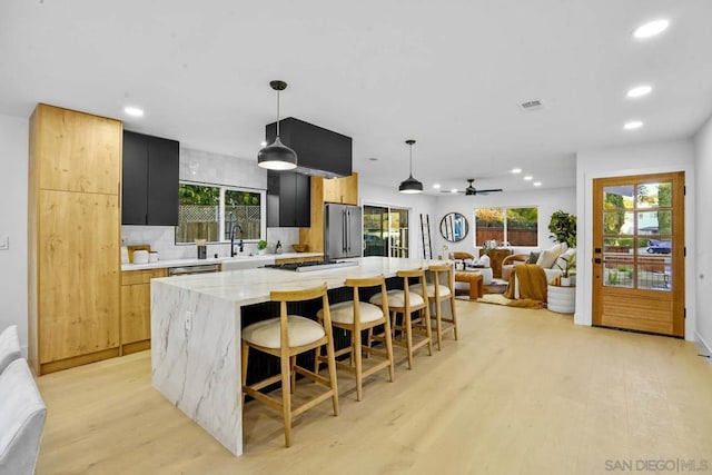 kitchen with appliances with stainless steel finishes, pendant lighting, a kitchen bar, a center island, and light stone countertops