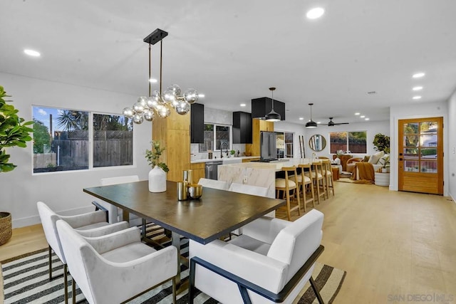 dining area with sink, ceiling fan with notable chandelier, and light hardwood / wood-style floors