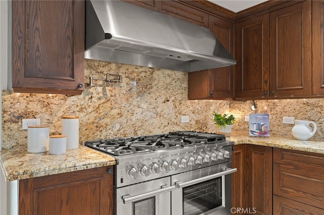 kitchen with light stone counters, wall chimney exhaust hood, range with two ovens, and backsplash