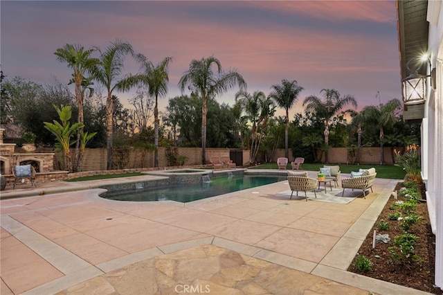 pool at dusk featuring an in ground hot tub, an outdoor stone fireplace, and a patio area