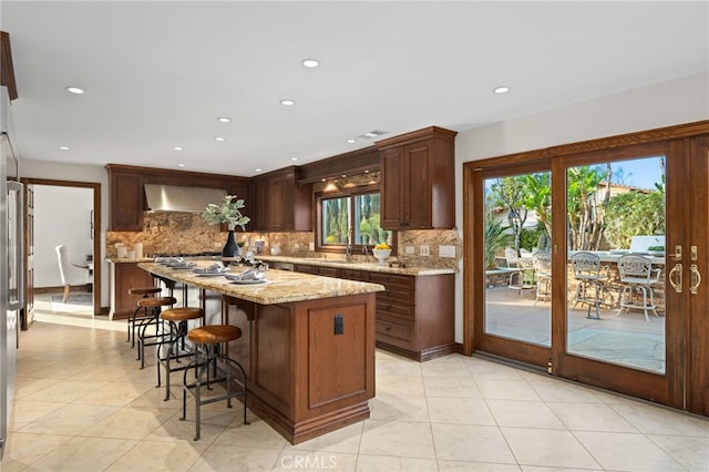 kitchen with light stone counters, wall chimney exhaust hood, a center island, and tasteful backsplash