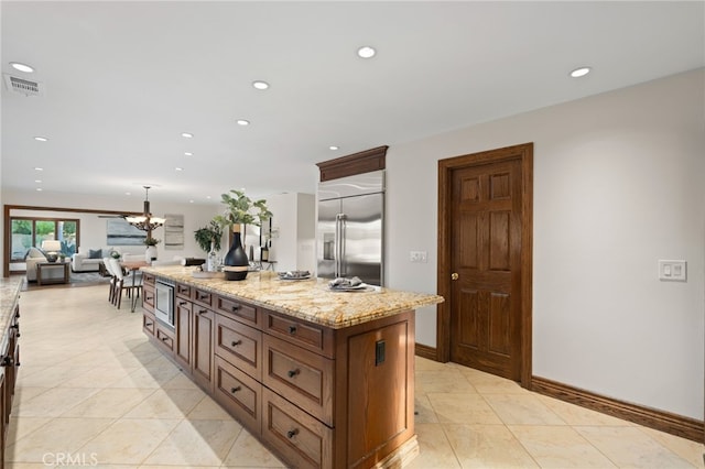 kitchen featuring light tile patterned flooring, light stone counters, built in appliances, a center island, and a notable chandelier