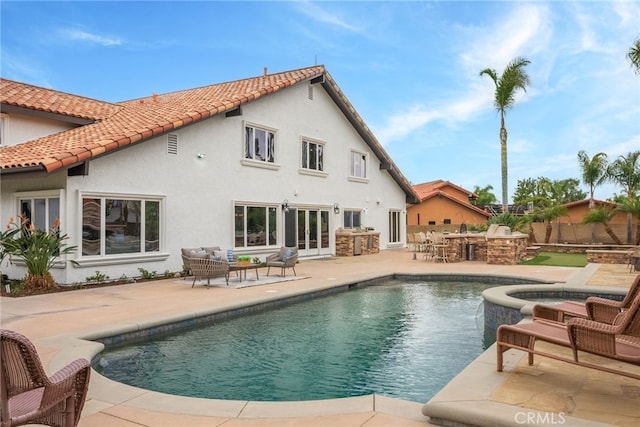 rear view of property with a bar, an outdoor kitchen, a swimming pool with hot tub, and a patio area