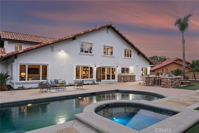 pool at dusk with an in ground hot tub, an outdoor kitchen, a patio, and a bar