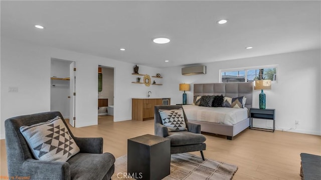 bedroom featuring a walk in closet, an AC wall unit, indoor wet bar, and light hardwood / wood-style flooring