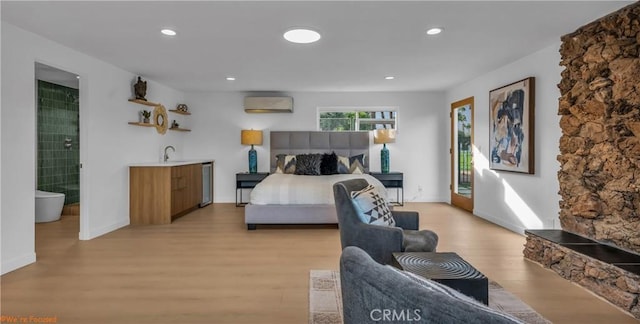 bedroom featuring connected bathroom, access to exterior, a wall mounted AC, and light wood-type flooring