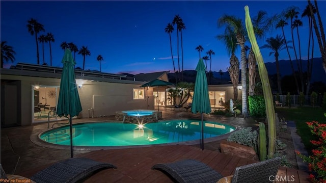 pool at twilight featuring a pool with connected hot tub and fence