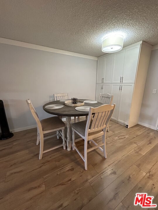 dining room with ornamental molding, a textured ceiling, and light hardwood / wood-style flooring