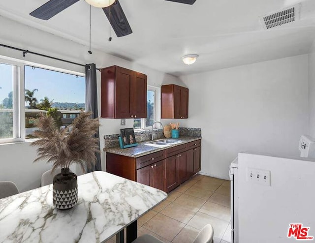 kitchen with light stone counters, sink, light tile patterned floors, and ceiling fan