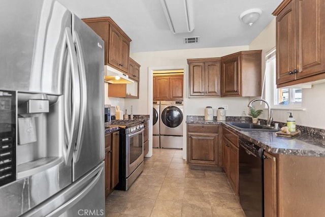 kitchen with sink, stainless steel appliances, washer and dryer, light tile patterned flooring, and dark stone counters