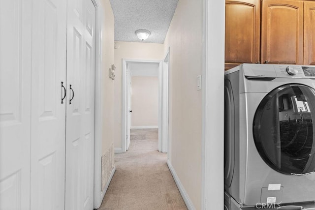 laundry room featuring washer / dryer, light colored carpet, cabinets, and a textured ceiling