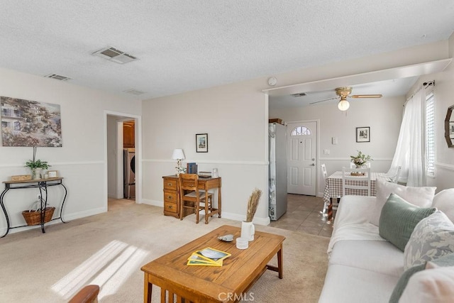 carpeted living room with ceiling fan, washer / dryer, and a textured ceiling