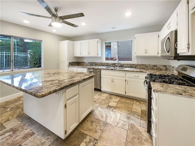 kitchen with sink, white cabinetry, stainless steel appliances, a center island, and dark stone counters