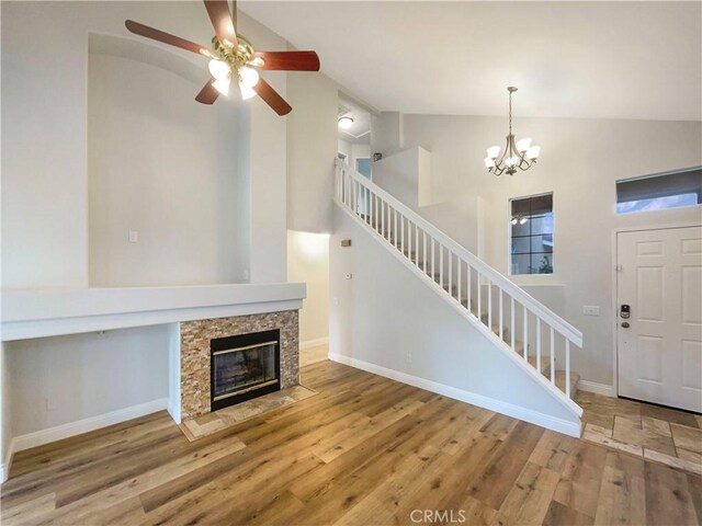 unfurnished living room featuring hardwood / wood-style flooring, a fireplace, ceiling fan with notable chandelier, and high vaulted ceiling