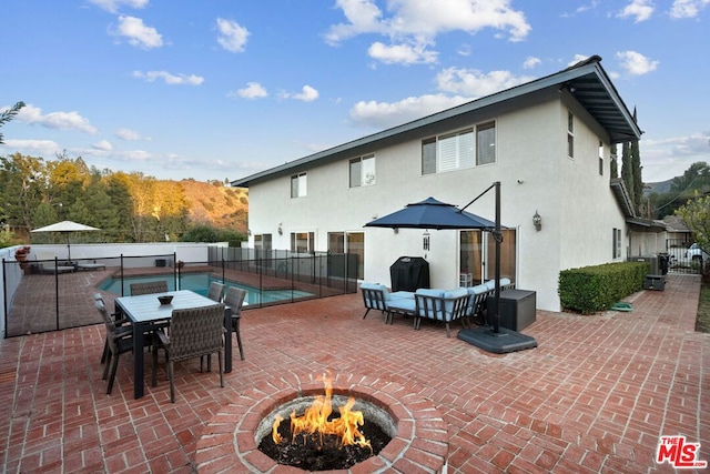 rear view of property featuring a fenced in pool, a patio area, and a fire pit