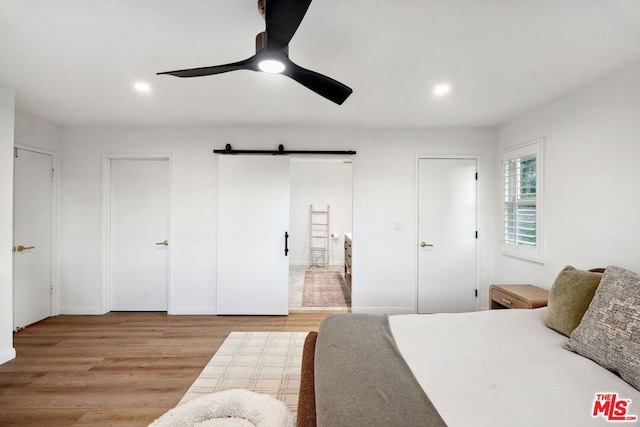 bedroom with a barn door, ceiling fan, and light hardwood / wood-style flooring