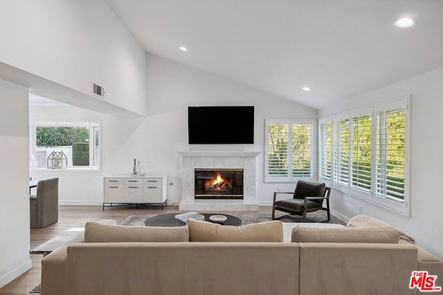 living room featuring a premium fireplace, high vaulted ceiling, and light hardwood / wood-style flooring