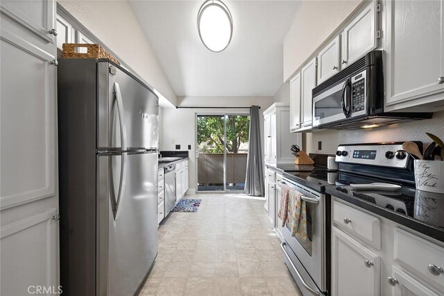 kitchen featuring white cabinetry, lofted ceiling, dark stone countertops, and appliances with stainless steel finishes