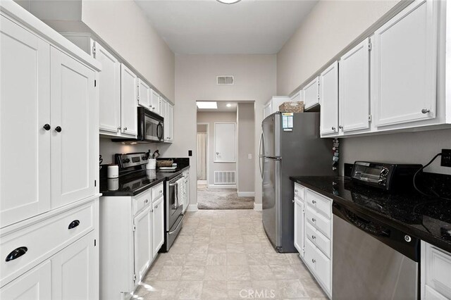 kitchen with stainless steel appliances, white cabinetry, and dark stone countertops