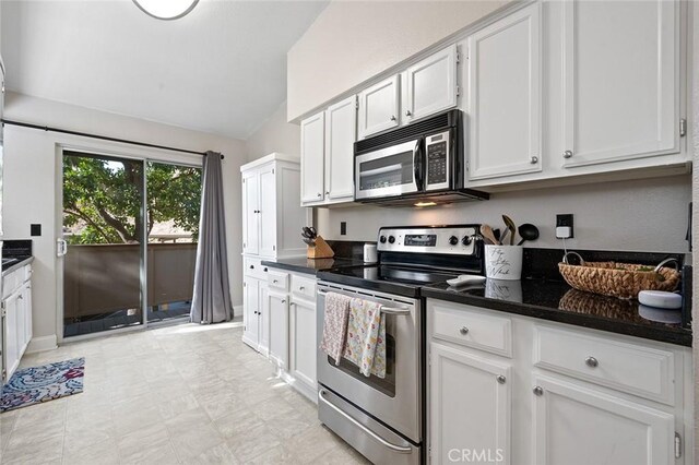 kitchen with white cabinetry, stainless steel appliances, dark stone counters, and lofted ceiling