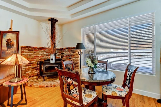 dining room with a raised ceiling, a wood stove, and light hardwood / wood-style floors