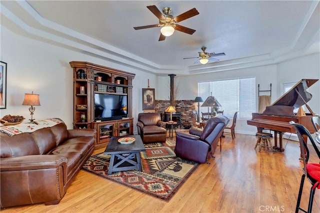 living room featuring ceiling fan, a tray ceiling, light hardwood / wood-style floors, and a wood stove