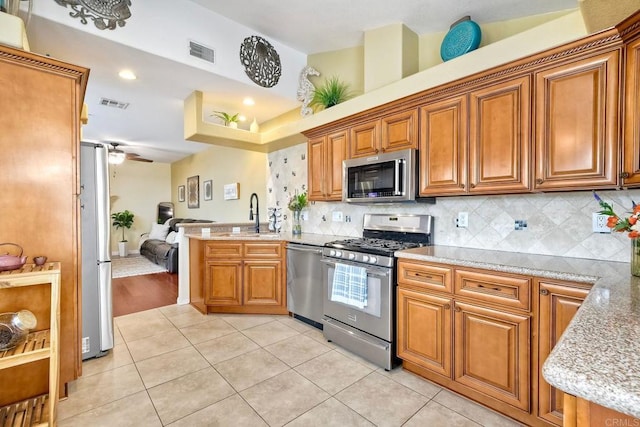 kitchen with light tile patterned flooring, sink, appliances with stainless steel finishes, light stone countertops, and decorative backsplash