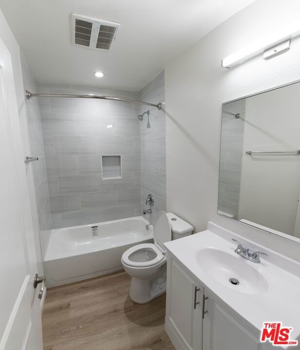 full bathroom featuring vanity, tiled shower / bath combo, wood-type flooring, and toilet