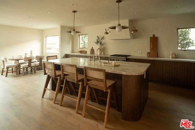 kitchen with sink, hanging light fixtures, stove, a kitchen island with sink, and light hardwood / wood-style floors