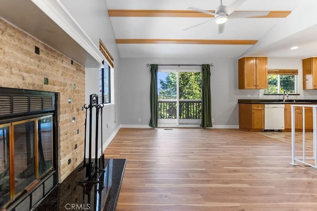 unfurnished living room featuring a fireplace, lofted ceiling, sink, ceiling fan, and light wood-type flooring