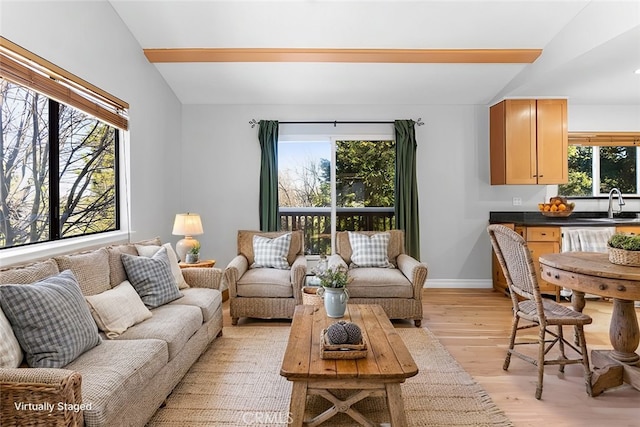 living room with lofted ceiling, a healthy amount of sunlight, sink, and light hardwood / wood-style floors