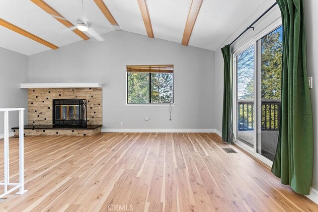 unfurnished living room with ceiling fan, a fireplace, lofted ceiling with beams, and wood-type flooring