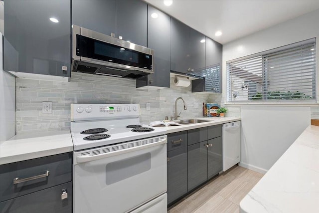 kitchen featuring sink, white appliances, gray cabinetry, tasteful backsplash, and light stone countertops