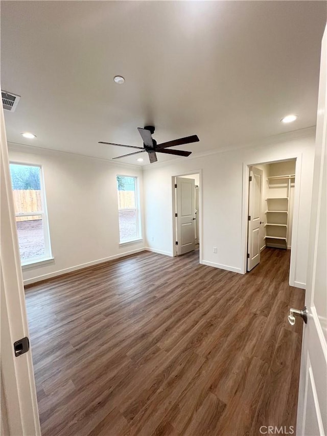 unfurnished bedroom featuring a walk in closet, dark wood-type flooring, and ceiling fan