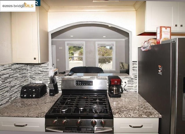 kitchen with white cabinetry, crown molding, light stone counters, appliances with stainless steel finishes, and backsplash