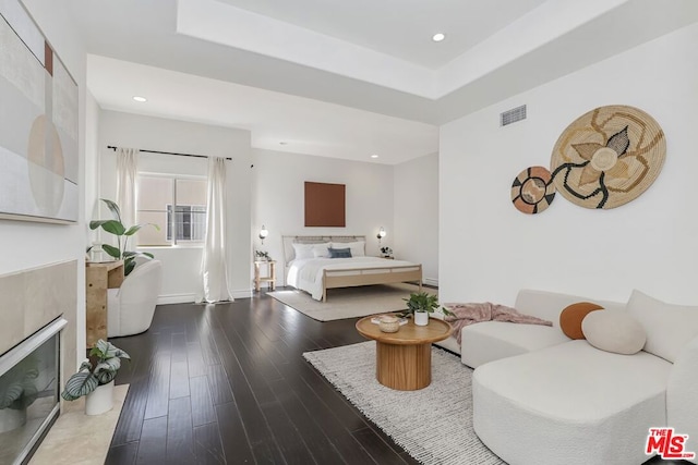 living room featuring hardwood / wood-style flooring, a tile fireplace, and a raised ceiling