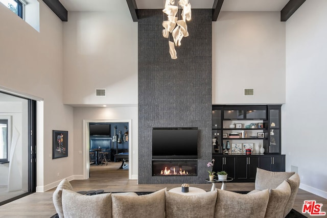 living room featuring beamed ceiling, wood-type flooring, a high ceiling, and a fireplace