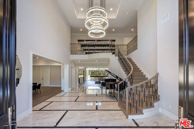 foyer entrance with an inviting chandelier, ornamental molding, a raised ceiling, and a high ceiling