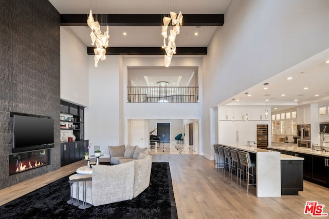 living room with beamed ceiling, a tile fireplace, a high ceiling, and light hardwood / wood-style flooring