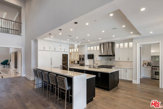 kitchen featuring wall chimney range hood, high end stainless steel range oven, hanging light fixtures, a spacious island, and white cabinets