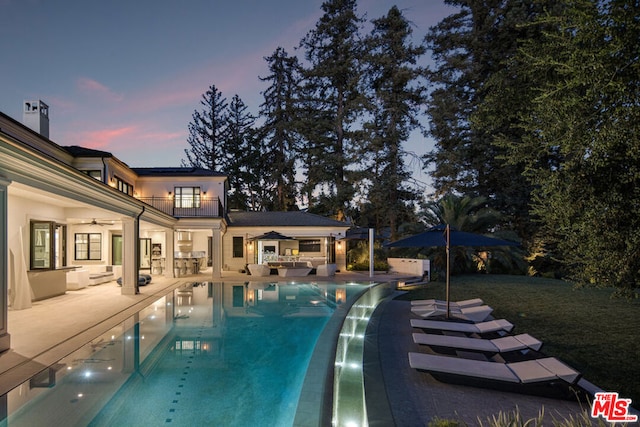 pool at dusk with ceiling fan, an outdoor living space, and a patio