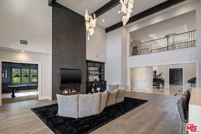 living room featuring billiards, a large fireplace, a high ceiling, beam ceiling, and light hardwood / wood-style flooring