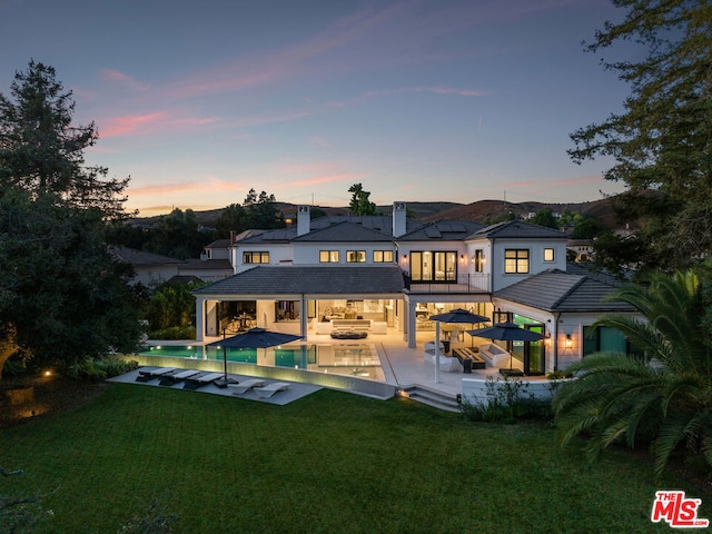 back house at dusk with an outdoor living space, a yard, and a patio area