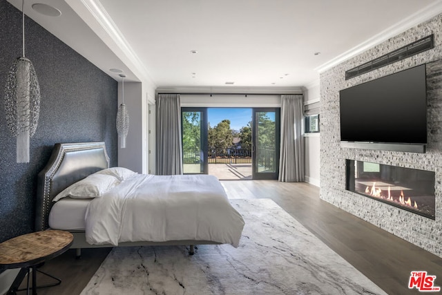 bedroom with crown molding, a large fireplace, hardwood / wood-style flooring, and access to outside