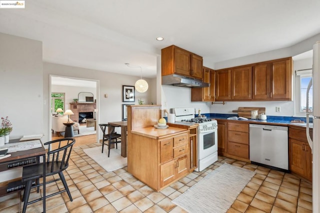 kitchen featuring light tile patterned flooring, white range with gas stovetop, a brick fireplace, dishwasher, and pendant lighting