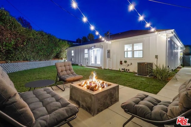 back house at night with a lawn, a fire pit, an outbuilding, central air condition unit, and a patio area